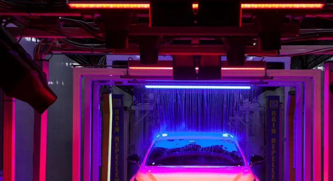 Inside a Quick Quack express wash tunnel with LED-lit equipment arches over a car